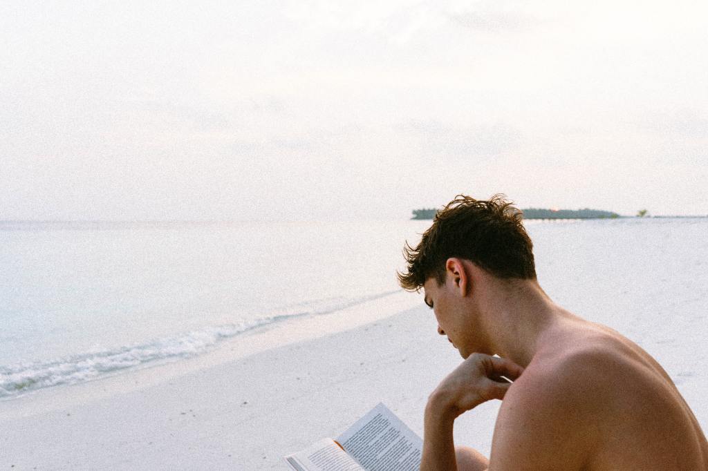 Lo-melanin young man on the beach reading a book